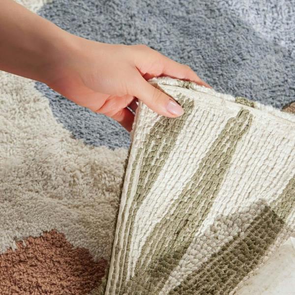 Close-up of a hand touching a textured rug with a neutral color palette.
