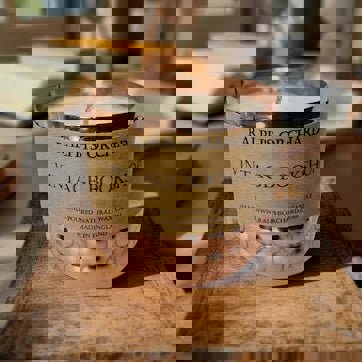 Candle in a decorative holder labeled 'Ralph's Orchard Vintage Bookshop' on a wooden surface.