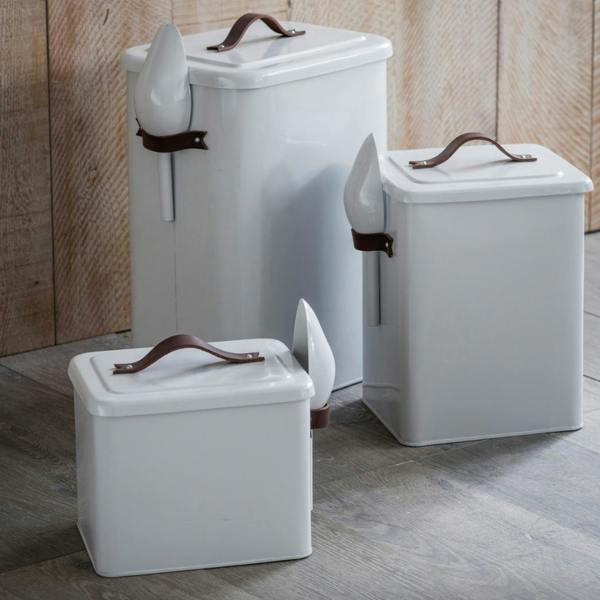 Three white chalk-coloured powder-coated steel pet bins in small, medium, and large sizes with leather handles and matching side scoops against a wooden background.
