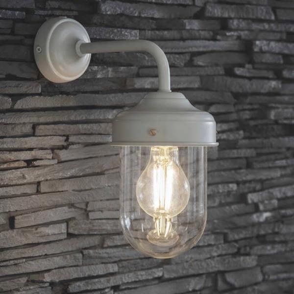 Wall mounted gloss clay barn light with a clear glass shade and glowing filament bulb on a grey stone wall.