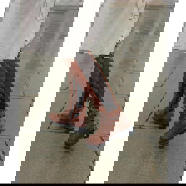 Hush Puppies Womens Vanessa Mid Calf Leather Boots, stylish mid-calf leather boots in brown with black side panels and ankle strap detail, worn by a person on a city sidewalk.