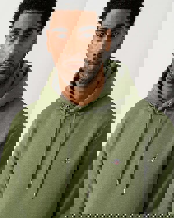 close up shot of a model wearing a GANT Mens Regular Fit Shield Logo Pullover Hoodie in 379 Dry Herb Green