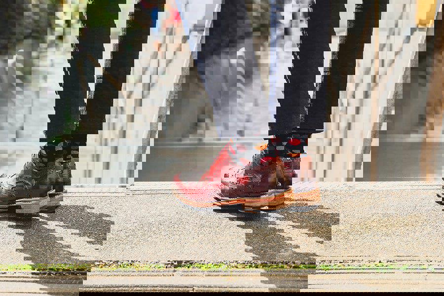 Person wearing red shoes and colorful cool socks standing on a sidewalk.