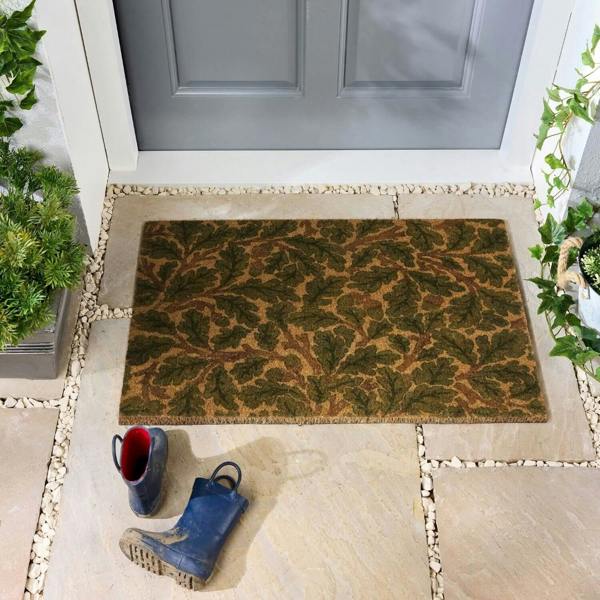 Doormat with leaf pattern on a stone pathway leading to a door, with boots and plants around.