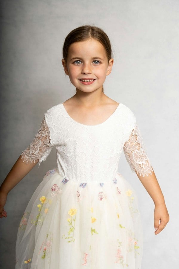 Young girl wearing a white dress with floral embroidery on a gray background