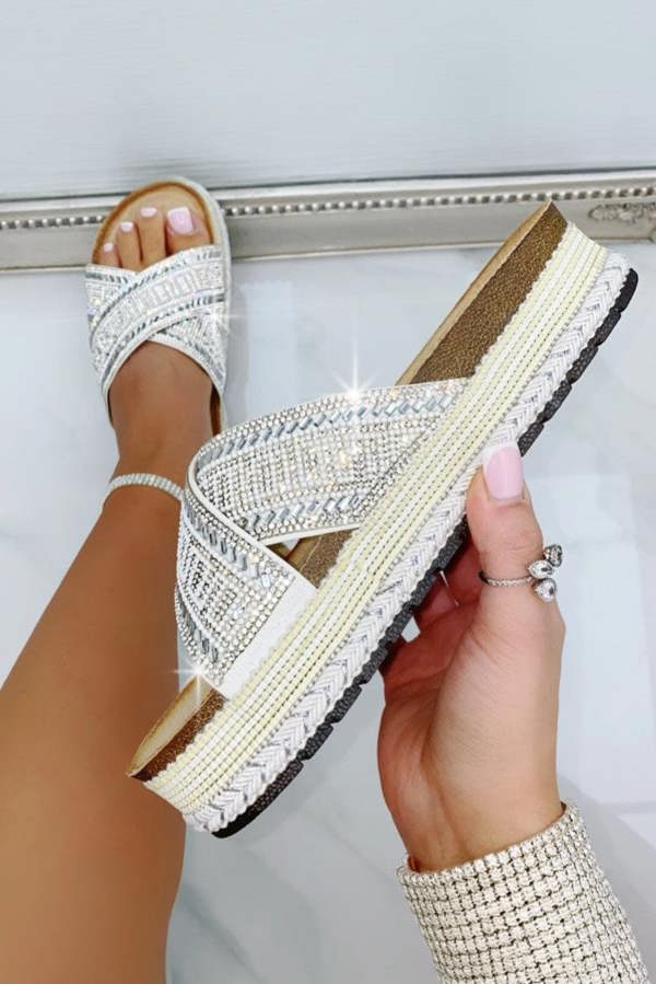 White sandal with criss-cross strap held by a hand against a light background