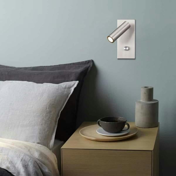 brushed nickel dimmable reading lamp mounted on the wall next to a bed with a side table 