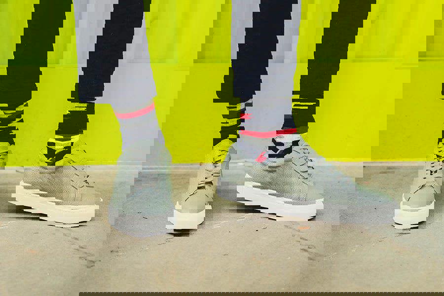 Gray sneakers worn with dark pants and colorful socks against a bright yellow background