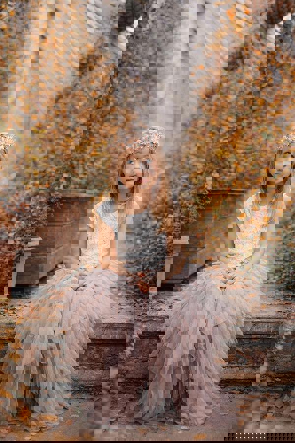 Young girl in a floral dress and headband walking through an autumn forest.