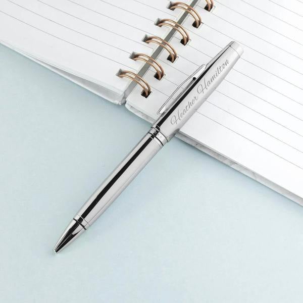 Personalised silver Cross Coventry ballpoint pen custom engraved with the name Heather Hamilton, resting on a white spiral notebook.