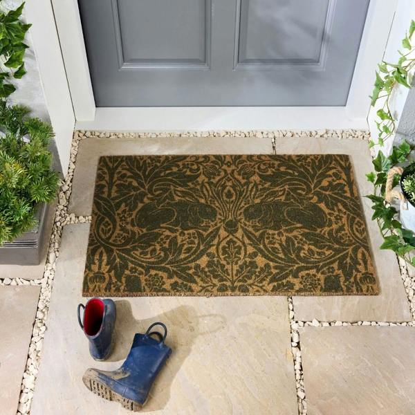 Decorative doormat with a floral pattern on a stone pathway leading to a door.
