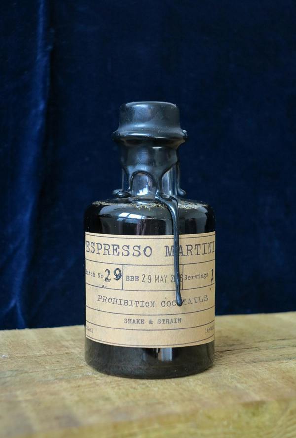 Vintage-style bottle with a label 'Espresso Martini' by 'Prohibition Cocktails' on a wooden surface and dark blue background.