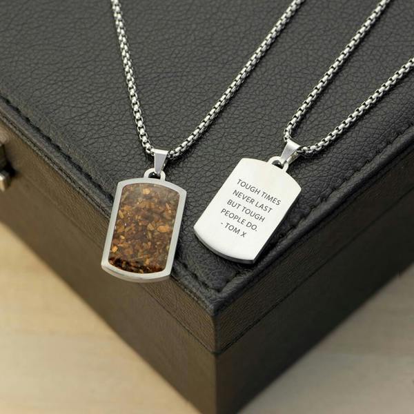 Two silver stainless steel dog tag necklaces on a black box, one showing a crushed brown tiger's eye stone inlay and the other showing a personalised engraved message.