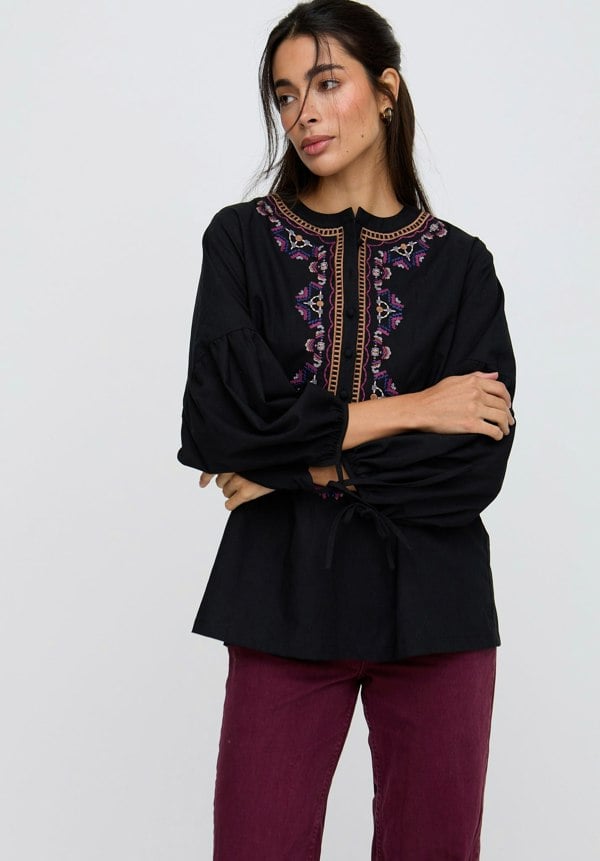 Woman wearing a black blouse with intricate purple embroidery on a white background