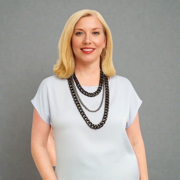 Woman wearing a white top and a tree tiered black aluminium and metal chain necklace a against a plain background