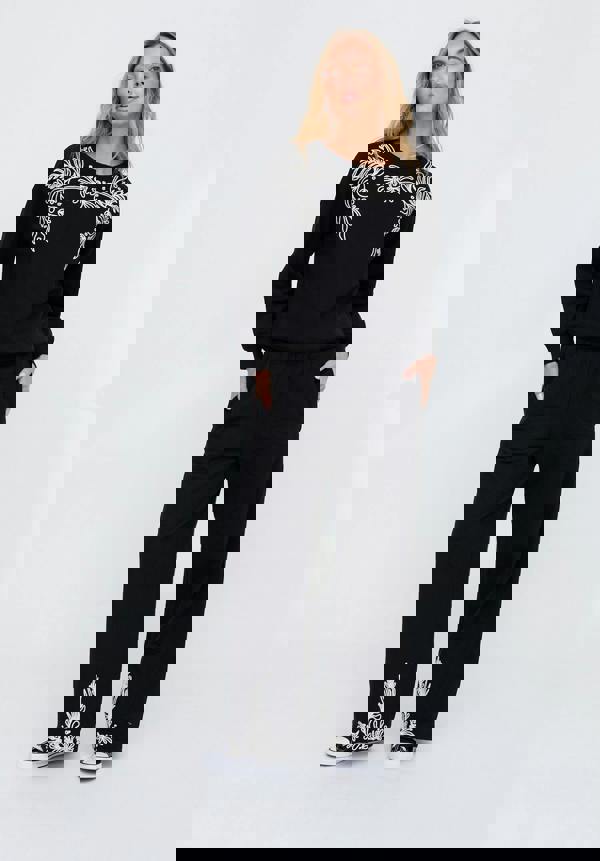 Woman wearing a black outfit with white embroidery on a white background