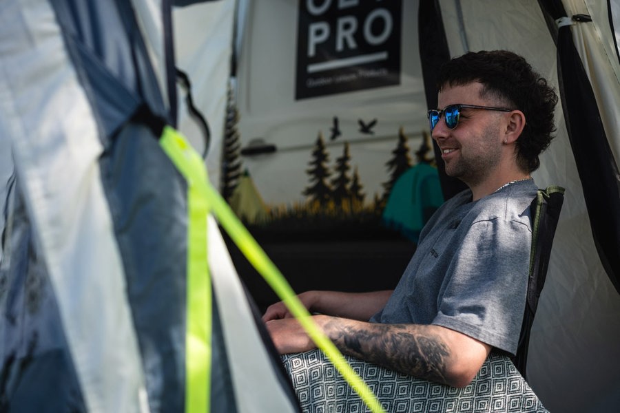 A man sits inside the Loopo Breeze® XL v2 Motorhome Awning by OLPRO, he is sat in a camping chair