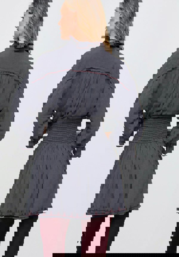 Woman wearing a gray dress with smocked waist and puffed sleeves on a light gray background