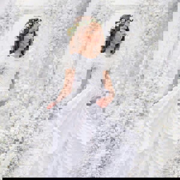 Young girl in a white dress standing against a floral background