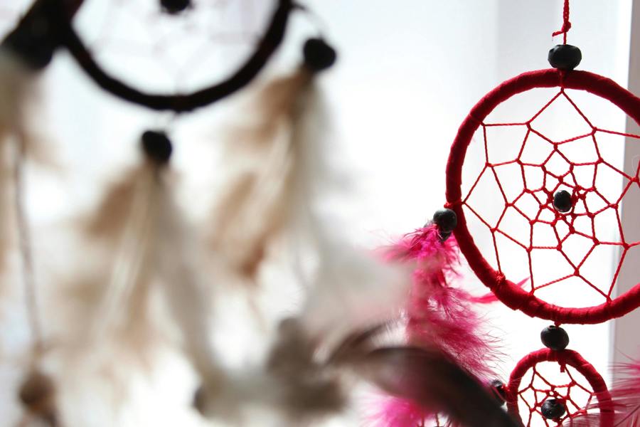 Red dreamcatcher hoop with web and bead center, with blurred cream feathers
