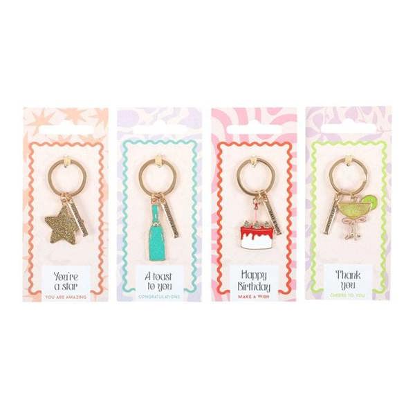 Four gold-tone keyrings with themed charms on colorful celebration card backing