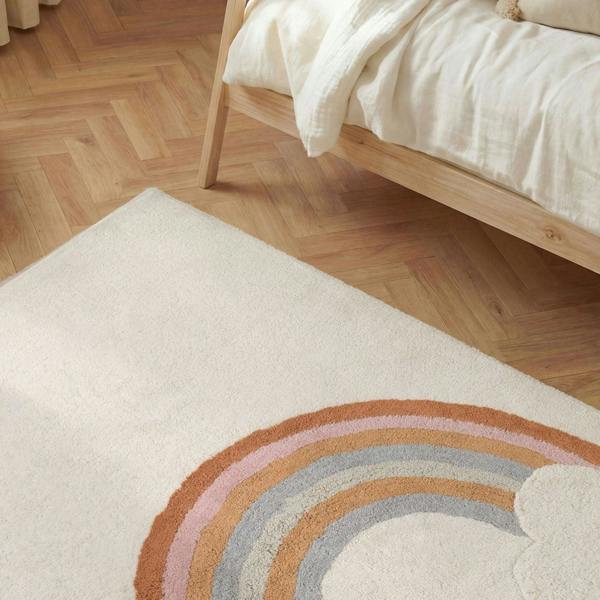 Beige rug with a rainbow design on a wooden floor next to a bed.