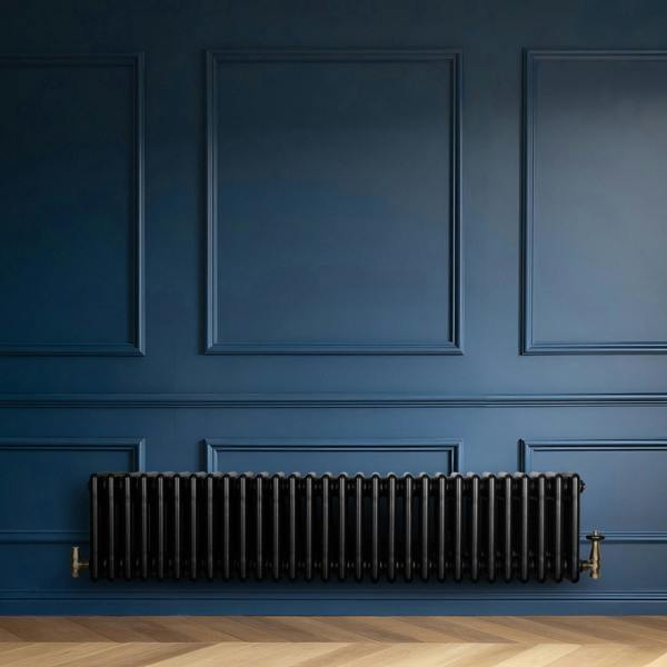 Traditional black 4 column radiator with brass valves, mounted on a deep blue wall, enhancing a modern interior design