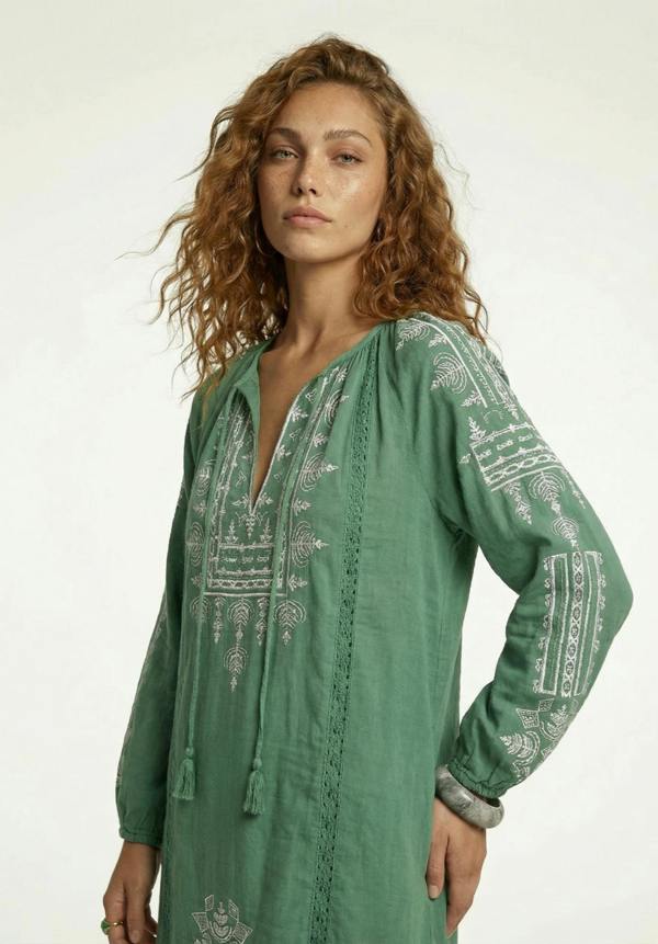 Woman wearing a green embroidered dress on a white background