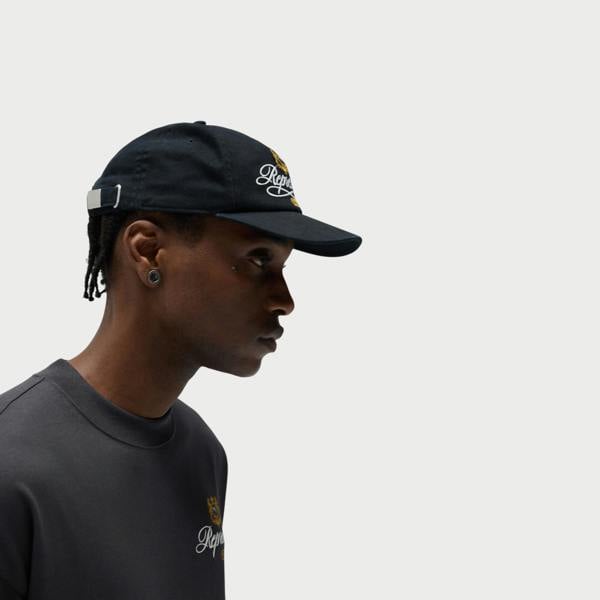 Supplied Fashion black baseball cap with embroidered logo crest worn by a man in profile view