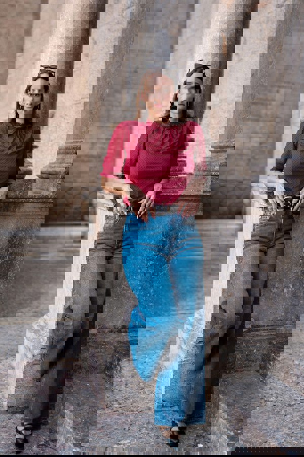 Woman in a red top and blue jeans standing on stone steps with columns in the background