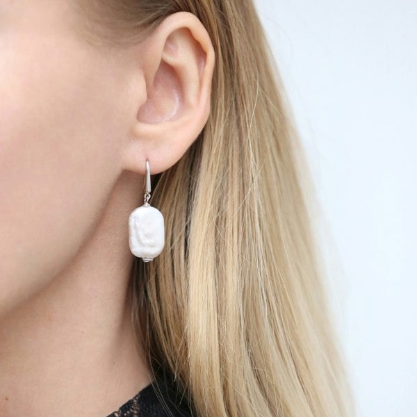 A close up of an ear with rectangle baroque pearl drop earrings.