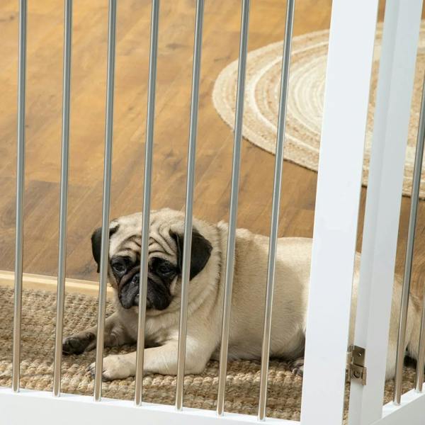 Pug lying behind white dog gate vertical bars on a rug
