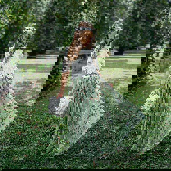 Young girl in a white and green dress standing in a park with trees and grass.