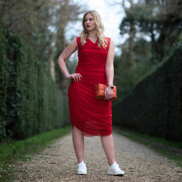 Women's Boudicca Summer Red Ruched Bodycon Midi Dress styled with an orange handbag and white sneakers for a chic, modern ensemble.