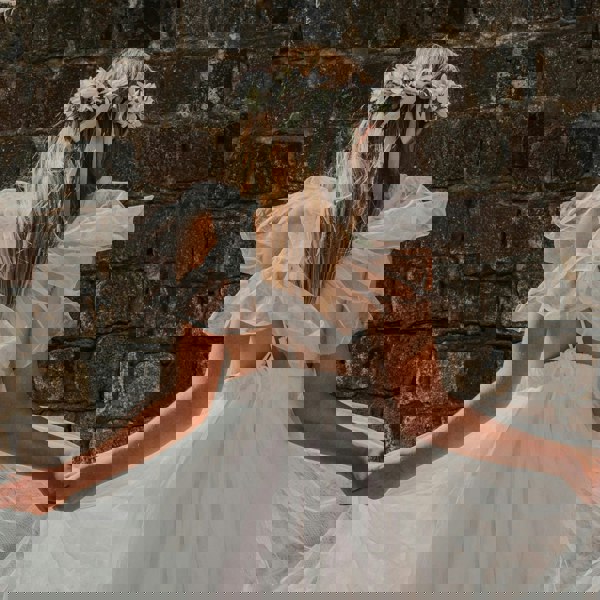 Girl in a white dress with ruffled sleeves standing against a brick wall.