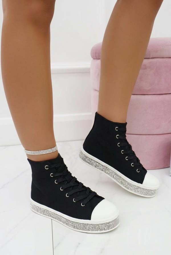 Black high-top sneakers with white soles worn by a person on a light background
