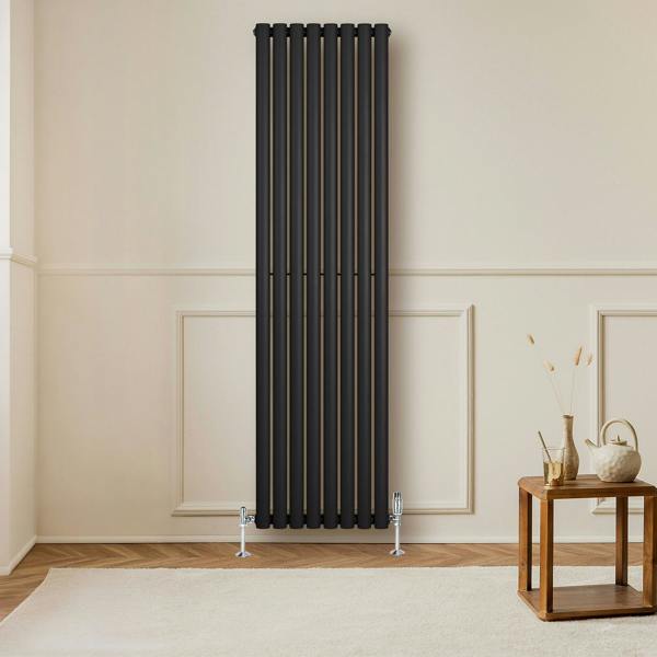 Sleek black oval single column radiator with vertical lines, mounted on a light wall, paired with stylish valves and wooden furniture