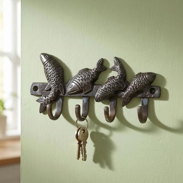 Close-up of a small cast iron fish hook mounted on a light green kitchen wall, showcasing detailed craftsmanship and functionality for hanging keys.