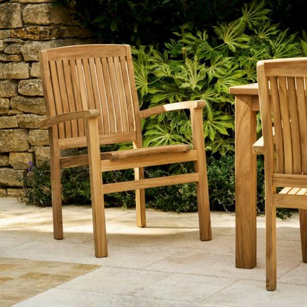 Solid teak carver garden armchair with ergonomic armrests and a multi-slatted backrest on a stone patio.