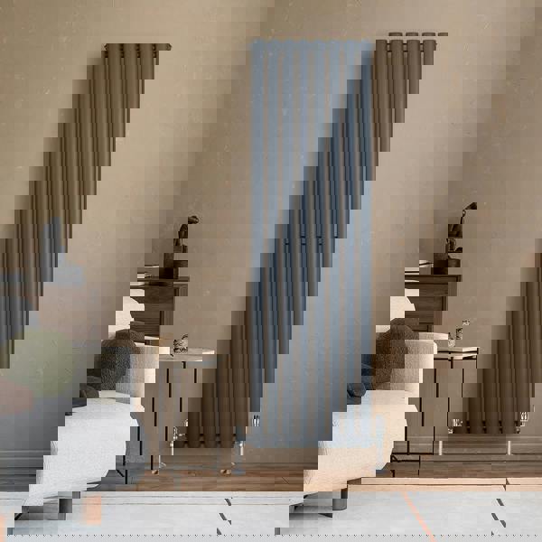 Anthracite grey oval single column radiator, 1600 x 480mm, mounted on a textured beige wall, complements modern living room decor