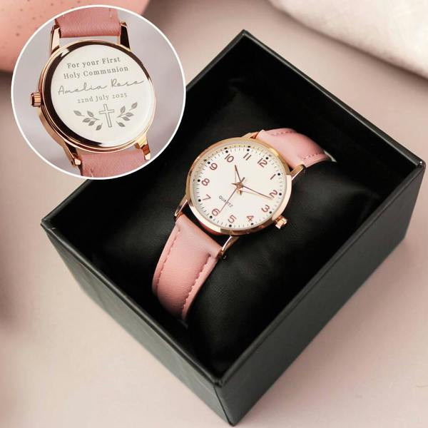 A child's personalised pink watch with a white face inside a black gift box, with a circular inset showing the custom engraved cross design on the back.
