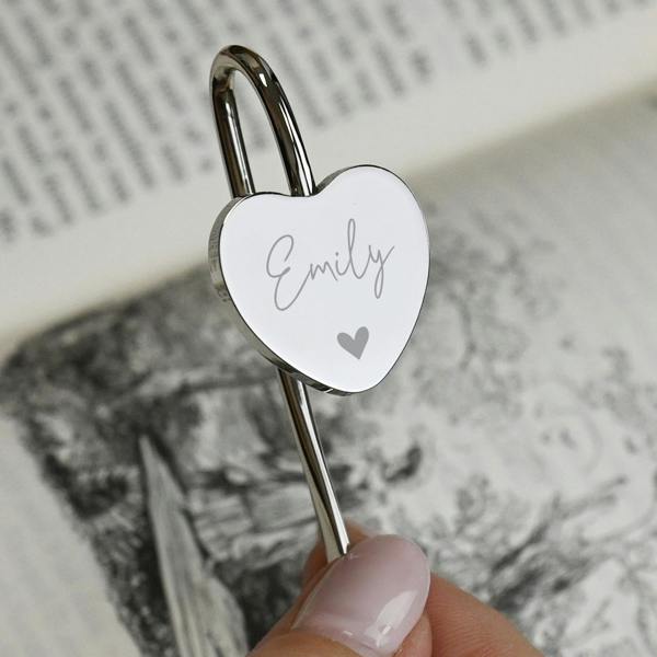 A polished silver-coloured heart bookmark engraved with the name Sophia in script text, marking a page inside an open book.