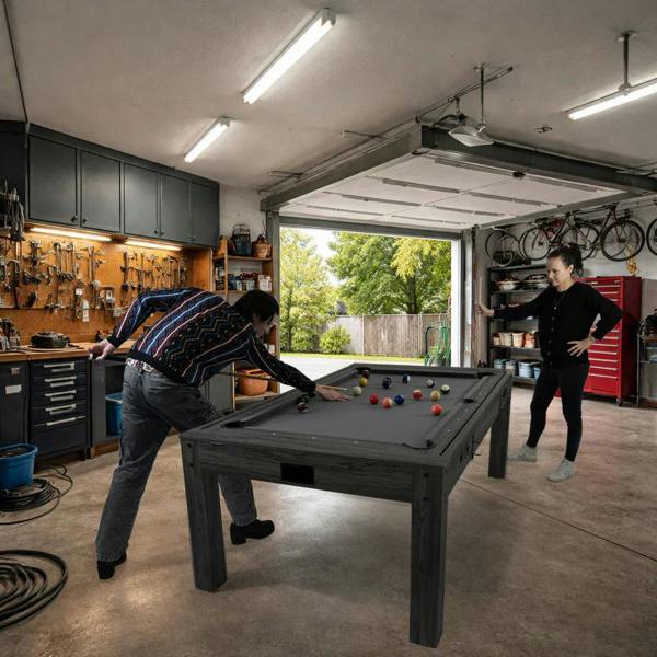 7-in-1 grey games table with a sleek design, featuring a billiards setup, darts, and LED lights, set in a garage environment