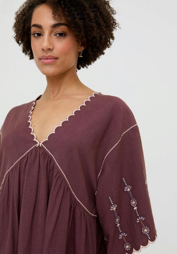 Woman wearing a purple dress with white embroidery on a plain background
