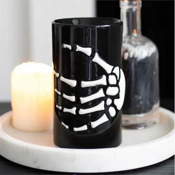 Black skeleton hand oil burner with white bone cutout, lit tealight flame inside