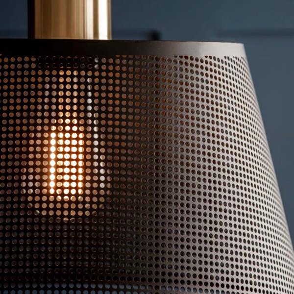 A tight close-up macro view focusing on the perforated matte black steel mesh and warm glowing bulb of an industrial pendant light by Abode Home & Gifts.