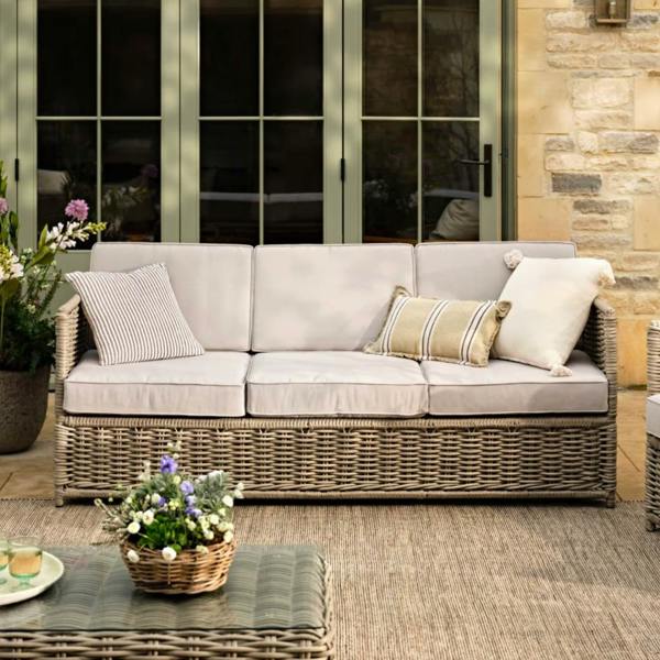Stone-coloured rattan 3-seater sofa with neutral cushions on a patio.