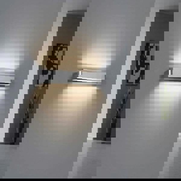 Silver up and down dimmable internal wall light on a grey background in a modern hallway