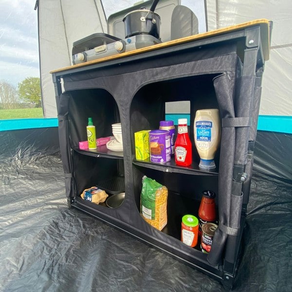 The OLPRO Deluxe Camp Kitchen With Double Cupboard pictured in a kitchen tent with cooking apparatus and food stored inside of it.