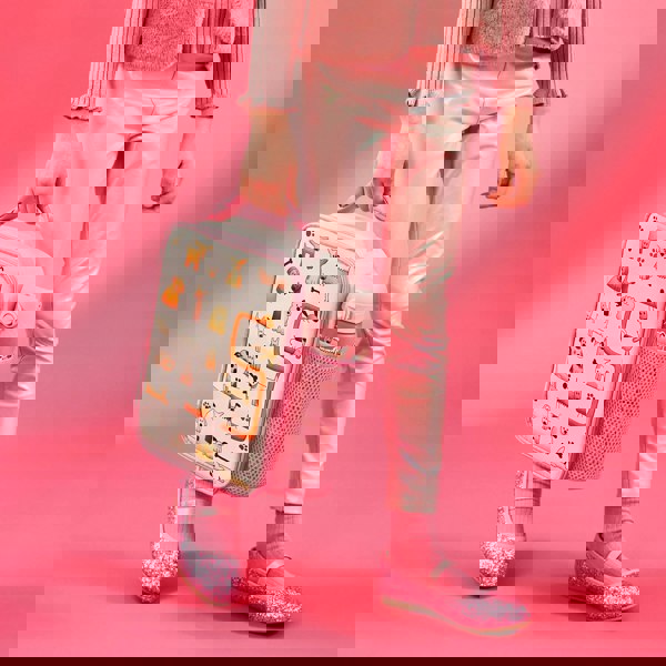 Person carrying a pink lunchbox decorated with cartoon dogs walking in a pink outfit including shiny leggings and glittery shoes against a pink background